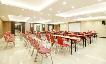 a large conference room with rows of red chairs arranged in a semicircle , and a projector screen mounted on the wall at Super OYO Collection O Sweet Karina Bandung