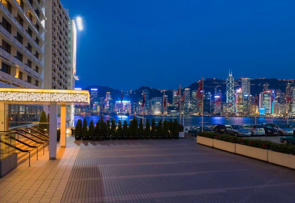 At the top floor level, there is a city at night with a lit-up skyline and water in front at Marco Polo Hongkong Hotel