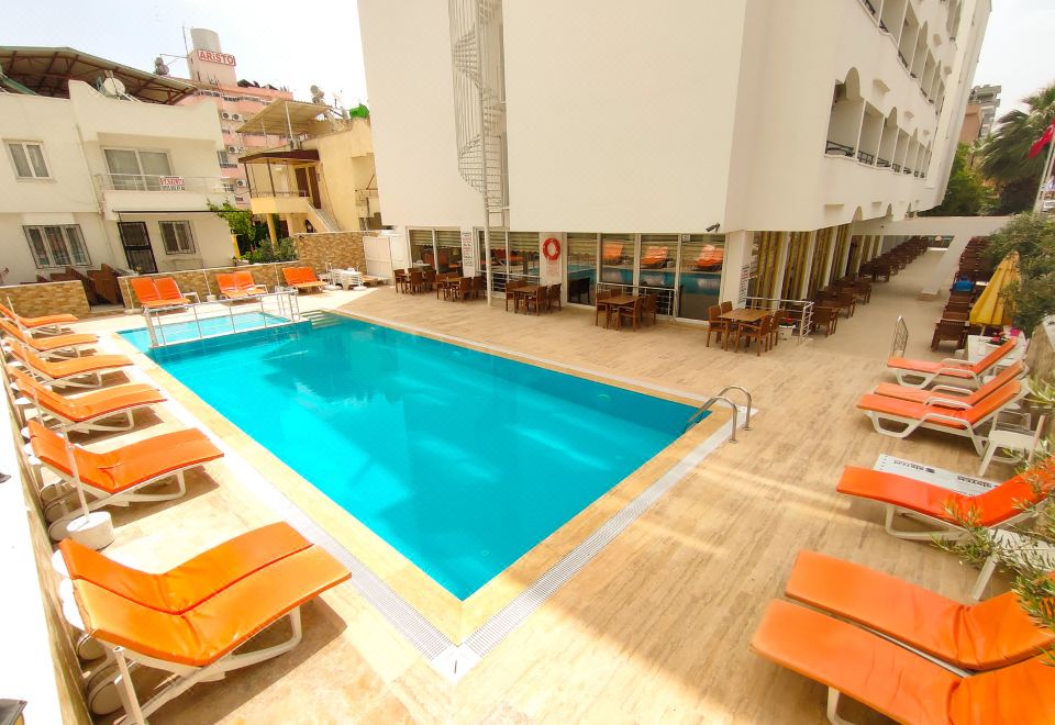 a large swimming pool surrounded by lounge chairs and umbrellas , with a hotel building in the background at Altinersan Hotel