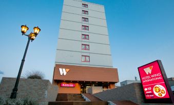 a large hotel with a tall tower and a red sign on the front of the building at Hotel Wing International Chitose