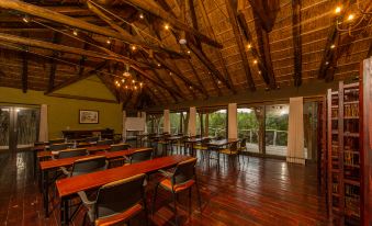 a large room with wooden floors and walls , containing multiple rows of tables and chairs , as well as tables with a red cloth at Pumba Private Game Reserve