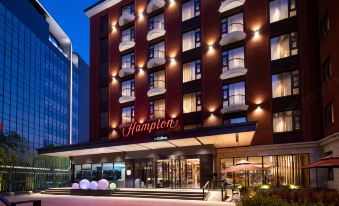 The rendering depicts a front view of the hotel at night, showcasing large windows and an outdoor dining area at Hampton by Hilton Beijing Guomao CBD