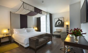 a large bed with a canopy is in the middle of a room with a chair and desk at NH Collection Santiago de Compostela