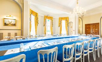 a long dining table with blue tablecloths and white chairs is set up in a room with yellow curtains at Woodland Manor Hotel