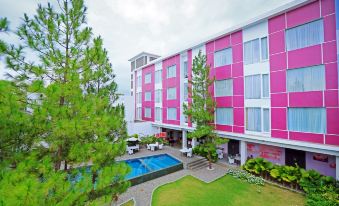 a pink and white building with a pool in front of it , surrounded by trees at Favehotel Cimanuk Garut