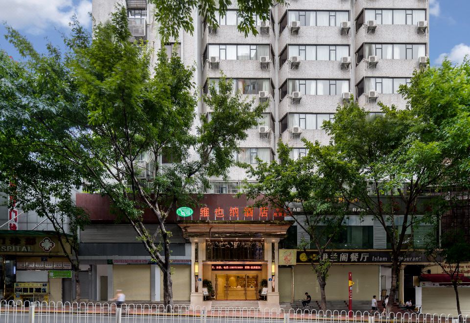 A large building with an entrance and trees in front of it on the sidewalk at Vienna Hotel (Guangzhou railway station & Xiaobei subway station)