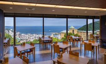 a restaurant with wooden tables and chairs , a view of the ocean through large windows at Kamenoi Hotel Atami Annex