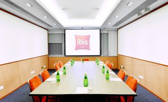 A conference room is set up with white walls, wooden tables, and chairs placed around the tables at Ibis Hong Kong North Point