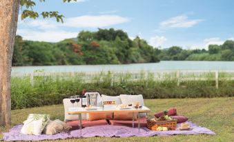 a picnic setup with a table , chairs , and various items on the ground near a lake at Dheva Mantra Resort