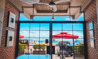 a room with a blue table and red umbrella , looking out onto the ocean through large windows at The Bricks Hotel