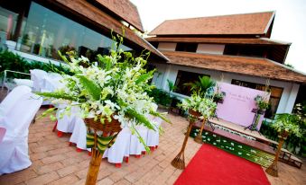 a wedding ceremony taking place in a courtyard , with multiple tables set up for guests at Parn Dhevi Riverside Resort & Spa