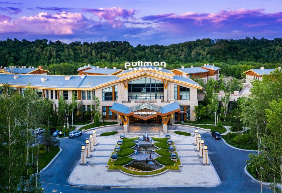 "an aerial view of a large building with the words "" pullman "" on its roof , surrounded by trees and a fountain" at Pullman Changbaishan Resort