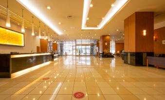 a large , well - lit lobby with a reception desk and chairs , as well as a red circle symbol on the floor at Hotel Kanazawa