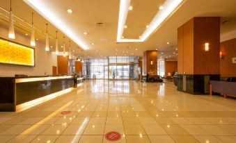 a large , empty hotel lobby with high ceilings , white tiles , and a reception desk , decorated with red and white flowers at Hotel Kanazawa