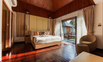 a spacious bedroom with a large bed , hardwood floors , and a sliding glass door leading to a patio at Kacha Resort & Spa, Koh Chang