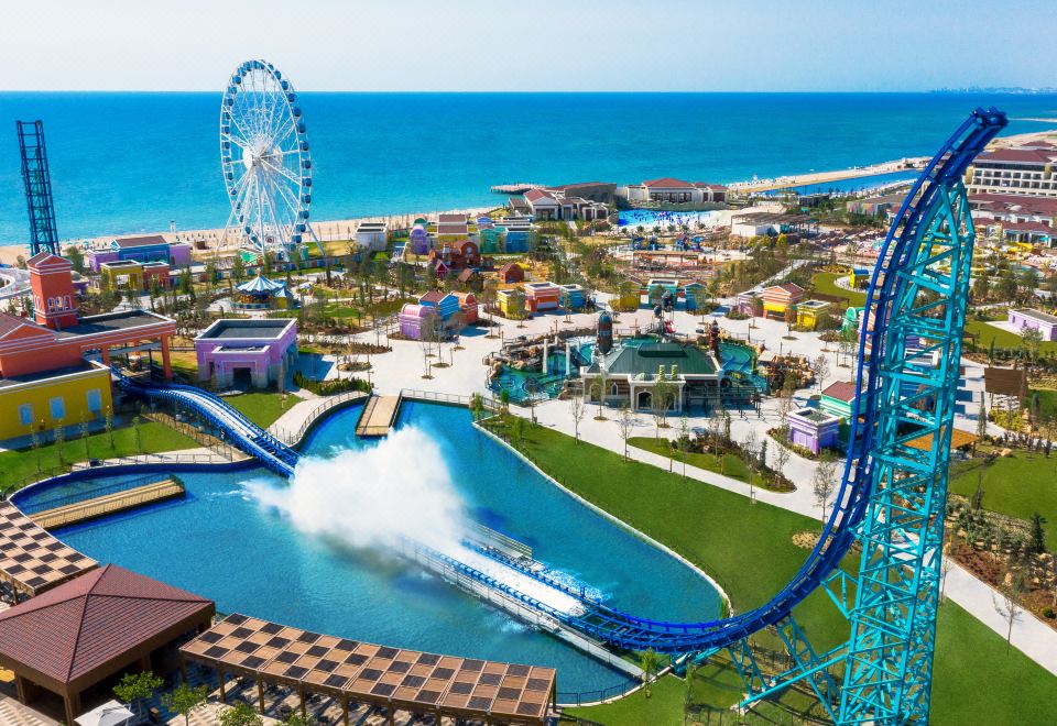 an aerial view of an amusement park with a roller coaster , water ride , and a ferris wheel at Rixos Water World Aktau