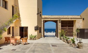 a courtyard with two chairs and a table , surrounded by a brick wall and a building with an open gate at La Tonnara di Bonagia Resort