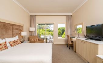 a well - lit hotel room with a large bed , a desk , and a window overlooking the outdoors at Joondalup Resort