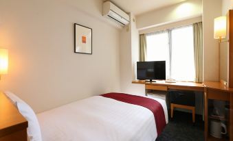 a bed with a white blanket and red blanket , next to a desk with a computer monitor at Hotel Hokke Club Hiroshima