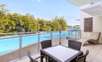 a balcony overlooking a pool and palm trees , with a dining table and chairs set up for a meal at Oaks Port Stephens Pacific Blue Resort