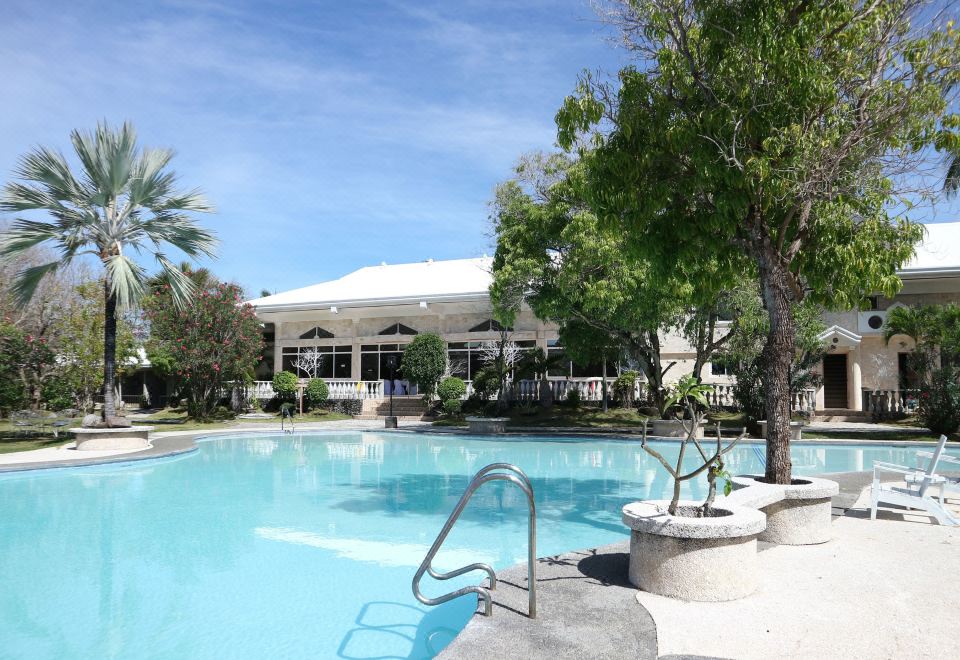 a large outdoor swimming pool surrounded by lush greenery , with a building in the background at Antulang Beach Resort