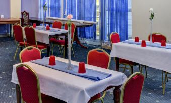 a dining room with red chairs and tables , white tablecloths , and blue curtains , providing a comfortable setting for guests at Empire Hotel