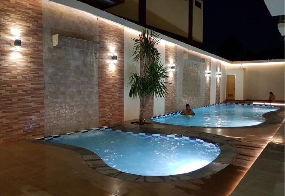 a man is relaxing in a hot tub with blue water , surrounded by a brick wall and lit up at night at Victoria Inn