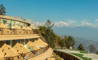 a large building with a balcony is situated on a hillside overlooking mountains and snow - capped peaks at Aagantuk Resort