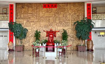 a large room with a statue of buddha on a pedestal and several potted plants in the foreground at Gushi Oriental Earl Hotel (Yucheng Avenue Genqin Culture Park)