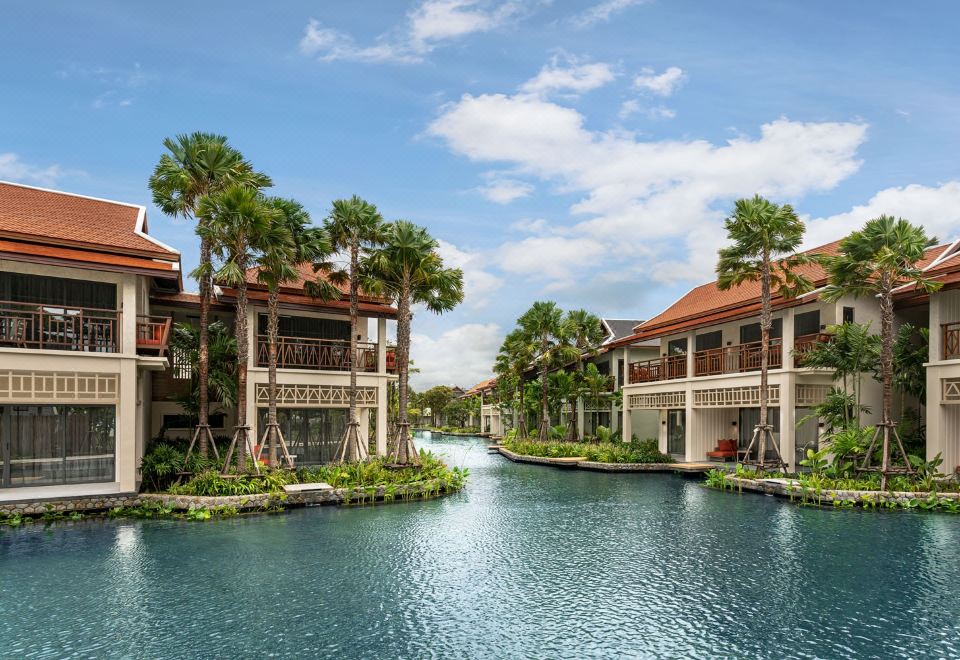 a beautiful waterfront property with palm trees , buildings , and a canal under a clear blue sky at Grand Mercure Khao Lak Bangsak