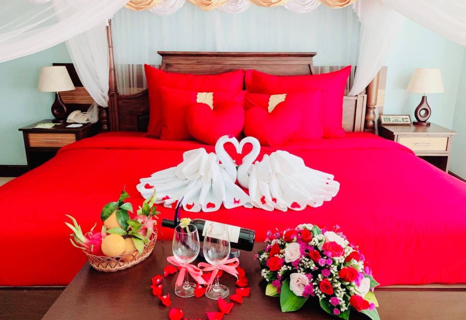 a romantic bedroom with a red bed , a tray of wine , and a heart - shaped towel on the bed at Golf Phu My Hotel