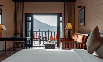 a hotel room with a large bed , two chairs , and a balcony overlooking the ocean at Atana Musandam Resort