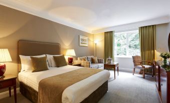 a large bed with a brown blanket and white sheets is in a room with a couch , chair , and window at Coldra Court Hotel by Celtic Manor