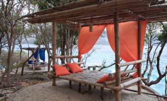 a wooden gazebo with orange cushions , surrounded by trees and a body of water , creating a serene outdoor space at Bluewater Sumilon Island Resort