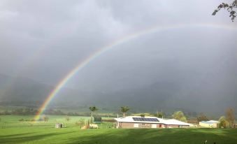 a beautiful rainbow arching over a lush green field , with the sky filled with overcast skies at Karelia Alpine Lodge