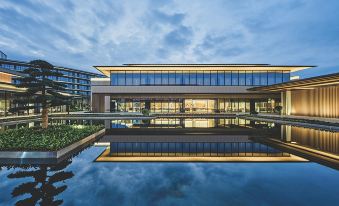At night, guests are treated to a breathtaking sight of a large building with glass panels reflecting on water, accompanied by an illuminated sign on top at NINGDE SANDU'AO FLIPORT HOTEL