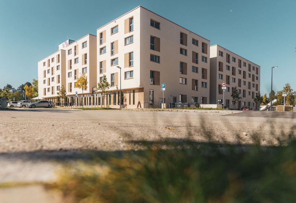 a large , modern building with multiple floors and balconies , situated in a parking lot surrounded by grass and trees at Maseven Muenchen Messe Dornach