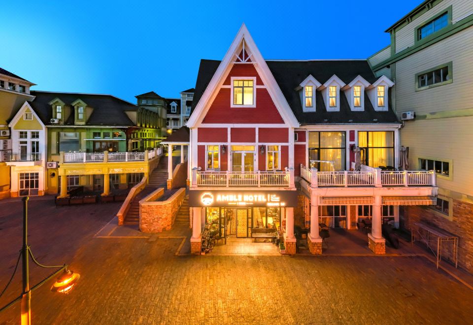 a red and white house with a balcony is lit up at night , surrounded by brick pathways at Amble Hotel