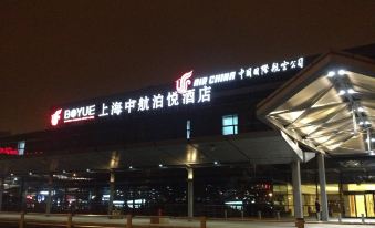 The entrance to a hotel is illuminated at night with a sign above it, surrounded by other buildings at Boyue Hotel Shanghai Air China Hongqiao Airport