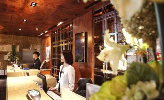 a woman is standing at a reception desk in a hotel lobby , interacting with the receptionist at M Hotels