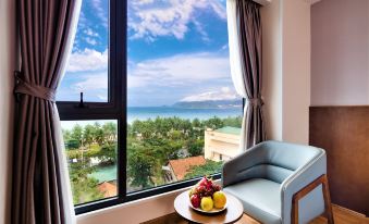 a room with a large window overlooking a body of water , featuring a couch , chairs , and a coffee table at DTX Hotel Nha Trang