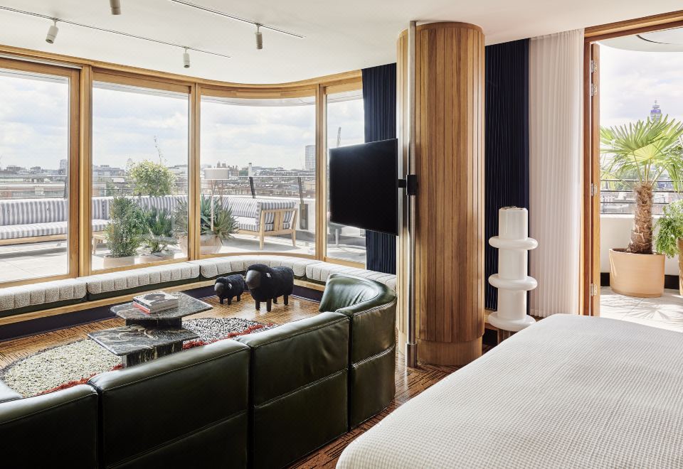 a modern living room with a large window , green leather sofa , and white round table , connected to a balcony view of a city at The Standard London