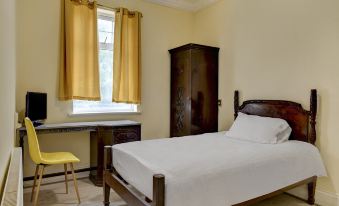 a bedroom with a bed , yellow curtains , and a tv on a wooden desk next to the window at Empire Hotel