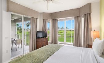 a well - furnished bedroom with a king - sized bed , a tv , and a view of a golf course outside the window at GreenLinks Golf Villas at Lely Resort