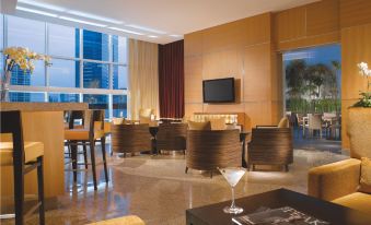 a modern , well - lit living room with large windows and wooden furniture , including sofas , chairs , tables , and a dining table at Oakwood Premier Cozmo Jakarta