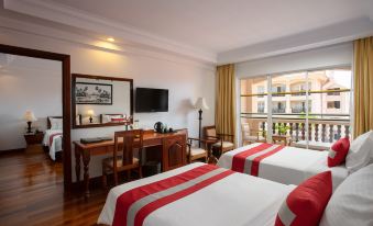 a hotel room with two beds , a desk , and a window , decorated in white and red colors at Hotel Somadevi Angkor Resort & Spa