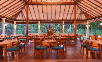 a large dining room with wooden tables and chairs , a chandelier , and a tree in the background at Adaaran Select Meedhupparu - with 24Hrs Premium All Inclusive