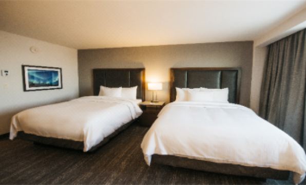 a hotel room with two beds , each made with white sheets and pillows , next to a nightstand with a lamp at The Explorer Hotel