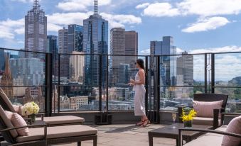 a woman is standing on a rooftop patio with a view of the city skyline at The Langham Melbourne