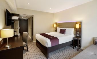 a large bed with a white and maroon blanket is in the middle of a room with a desk , chairs , and lamps at Premier Inn Honiton